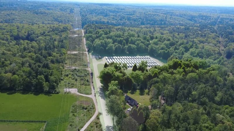 A rendering of the battery storage site as currently designed, from a distance: the battery yard in the woods beside the transmission line corridor, with forest and fields around it