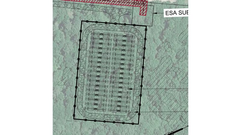 Two columns of battery units in rows inside a rectangular fence, ringed by a gravel fire lane, with the project substation at the top right where the gen-tie begins